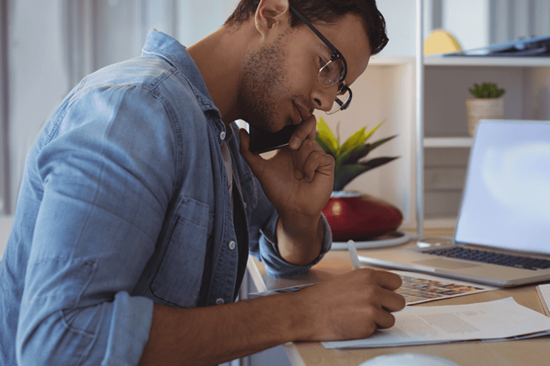 Man writing an inaccurate late payment removal letter while reviewing credit documents and speaking on the phone.