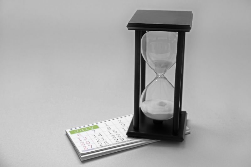 Hourglass placed beside a calendar, symbolizing the waiting period after sending a goodwill letter to a creditor for late payment removal from a credit report.