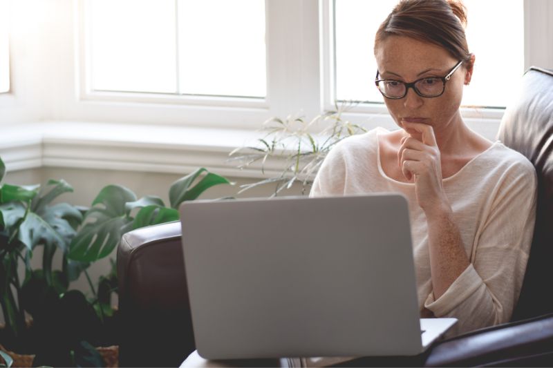 A woman sitting in a cozy room reviewing her credit information on a laptop, representing someone learning how to use DIY credit repair software at home to dispute credit report errors.