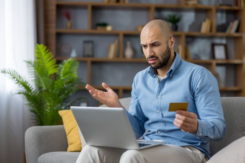 Frustrated consumer with declined credit card using laptop, representing credit repair law violations, FTC enforcement credit repair actions, and permanent ban on credit repair companies for illegal practices