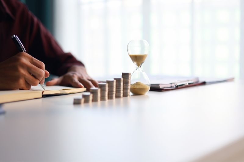 Person writing notes next to coins and hourglass representing credit repair laws that govern timing and reporting of disputes, including FCRA 30-day investigation requirement and credit bureau dispute rights