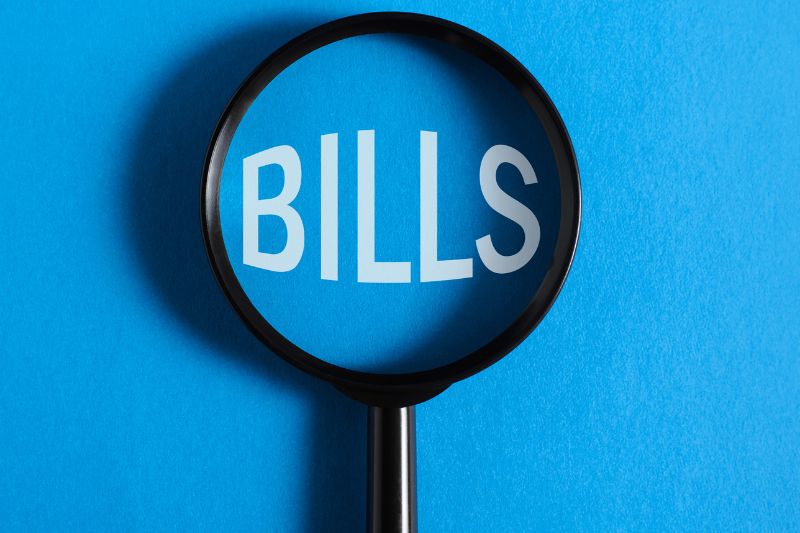 Magnifying glass over bills representing how credit repair laws protect consumers from unfair billing practices, including TSR advance fee ban and FDCPA rules on debt collection and charges