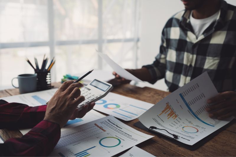 Team reviewing financial reports and calculator showing how legal regulations influence credit repair pricing models, including CROA advance fee rules, Telemarketing Sales Rule, and compliant service fees