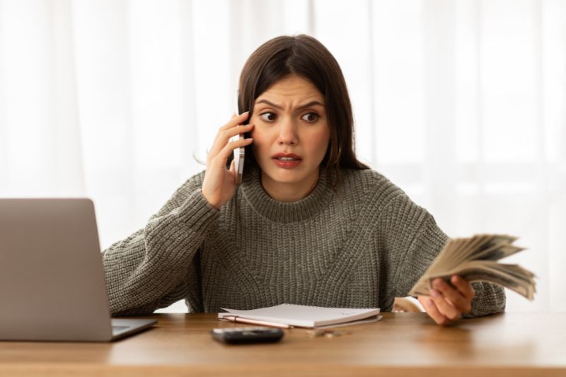 Concerned woman on phone reviewing finances, representing who to contact if a credit repair company is violating the law including FTC and CFPB complaint options