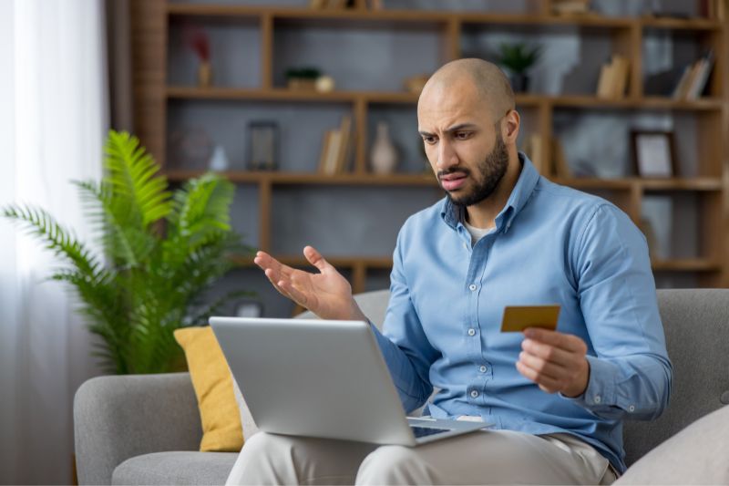 Frustrated man reviewing laptop and credit card after credit report dispute denied, showing common reasons why credit bureaus reject disputes and dispute rejected by credit bureau