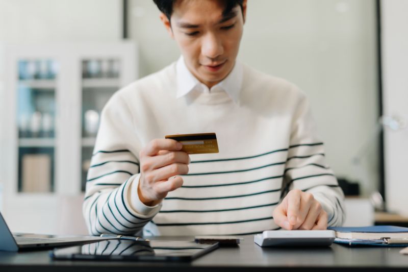 Consumer reviewing a credit card and calculating expenses while learning whether credit repair companies can charge upfront fees under CROA compliance laws
