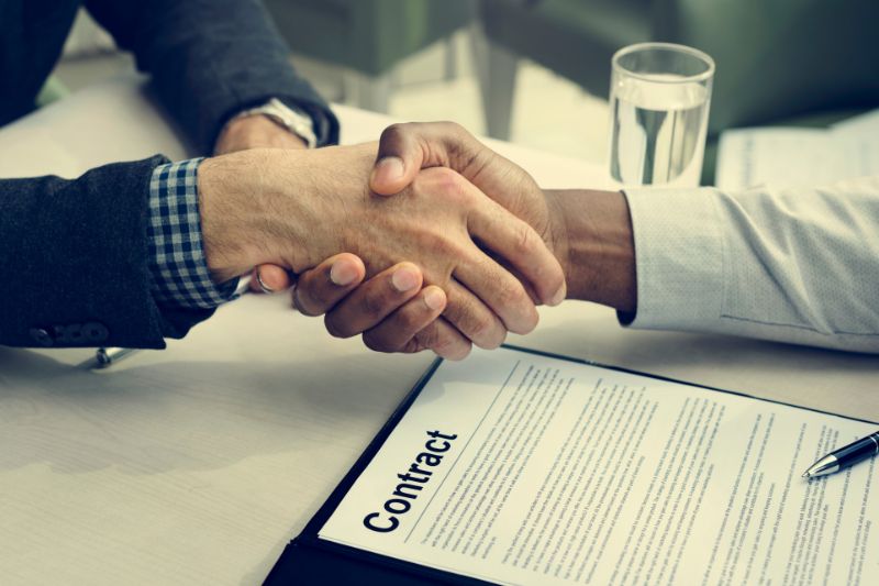 Business handshake over a signed contract representing written contract requirements under CROA for credit repair services and pricing compliance