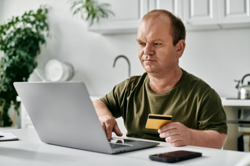 Man using a laptop and credit card while managing hybrid and subscription credit repair business models for ongoing monitoring and dispute services.