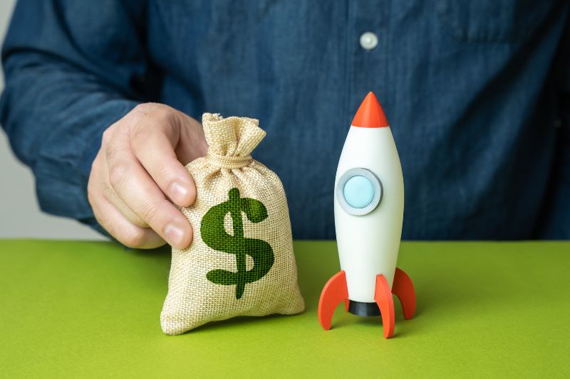 Money bag beside a startup rocket representing optional startup costs for a credit repair business.